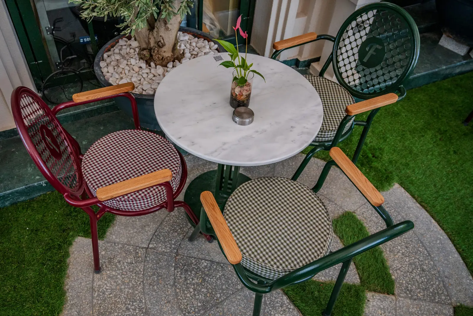 Mermer masa etrafında bordo ve yeşil kafe sandalyeleri, kaz ayağı desenli yuvarlak minderlerle