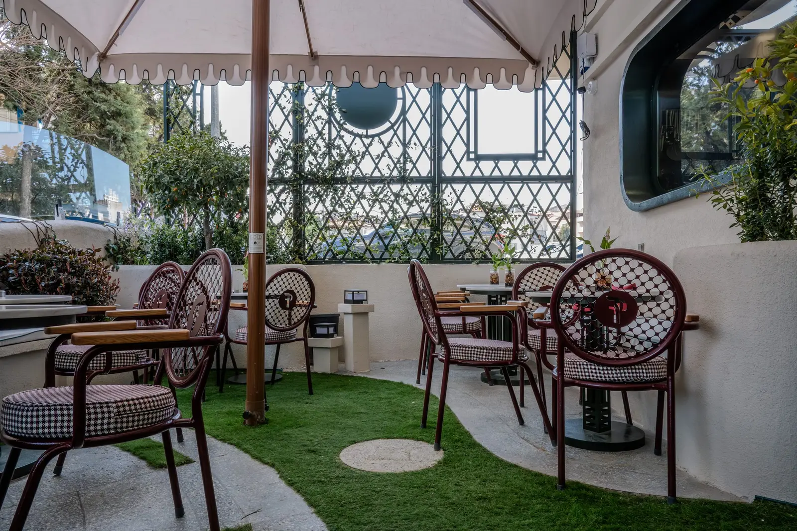 Tente altında bordo boyalı kafe sandalyeleri, üzerlerinde kaz ayağı desenli yuvarlak minderler